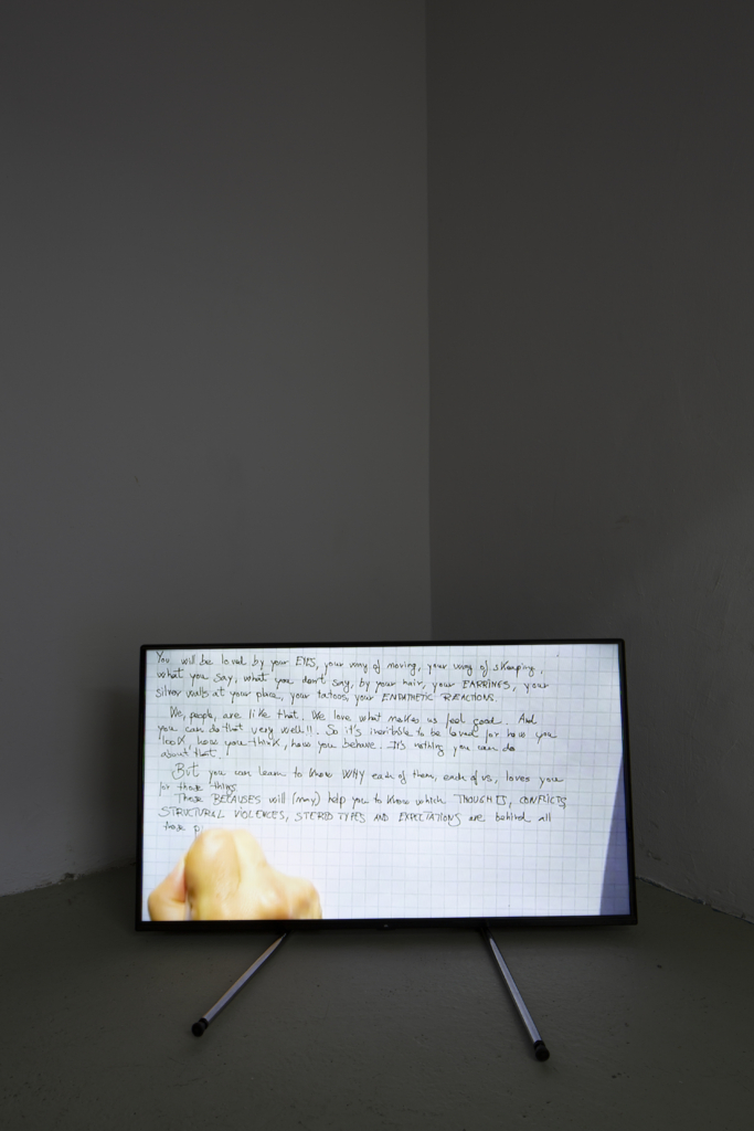 Frontalansicht eines am Boden stehenden Bildschirms, der eine Hand beim Schreiben zeigt.