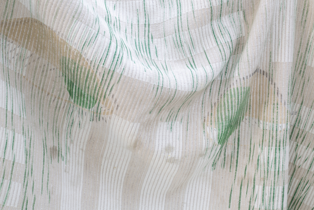Nahansicht eines mit grünem Siebdruck bedruckten gerafft hängenden beigen Teppichs.
