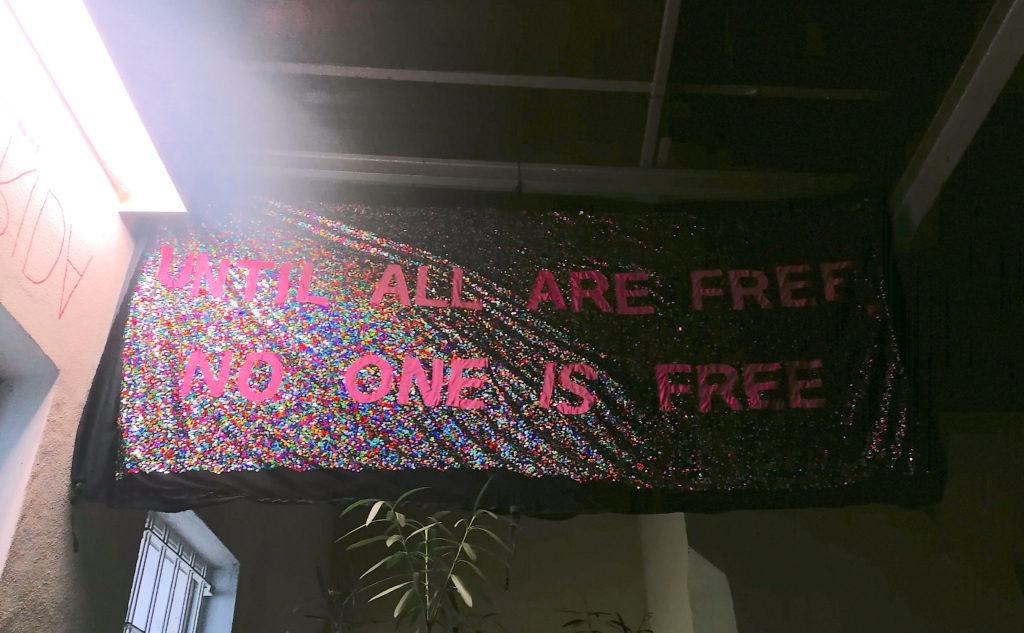 Ein glitzerndes Banner an der Pforte zur Lothringer 13: Until all are free no one is free.