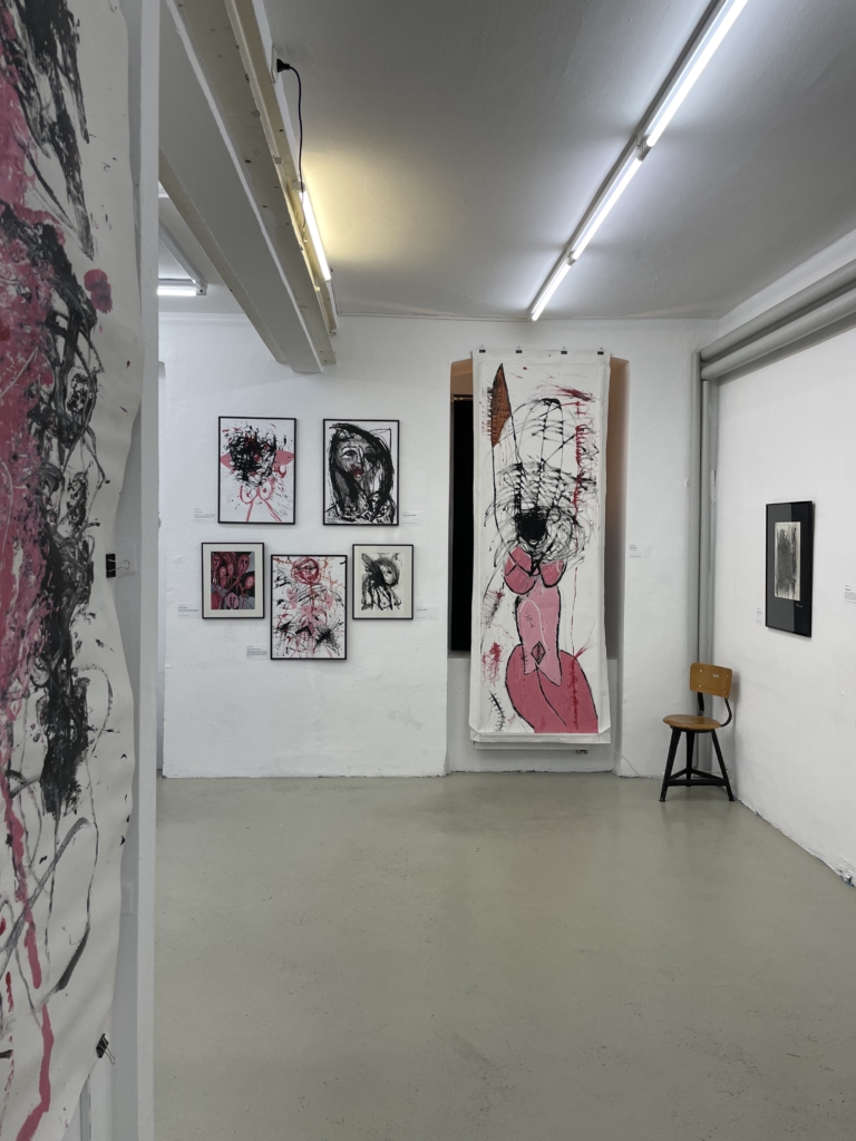 Ausstellungsansicht mehrerer Gemälde im raum. Sie zeigen wild expressive Körper in schwarz und rosa, teilweise mit Busen.