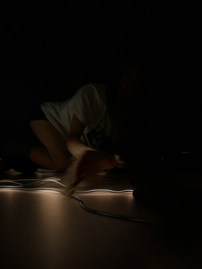 A Dark Room with the artist Citytronix performing on the floor with long light stripes layed out across the floor.