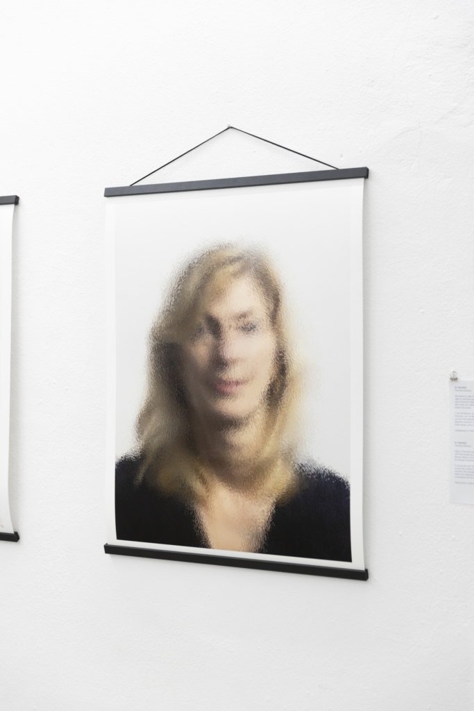 Nahaufnahme einer unscharfen Portrait-Fotografie einer blonden Frau, die wie Pergament einrollbar ist. Hängend an der Wand.